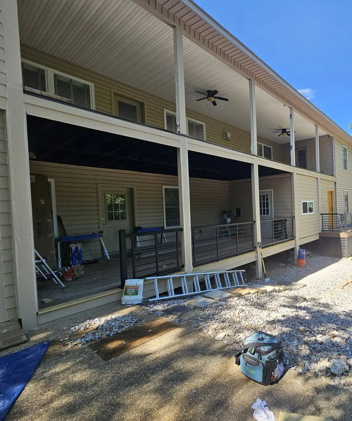 After: lower level finished in tan siding with new windows, a door opening and black cable railing.