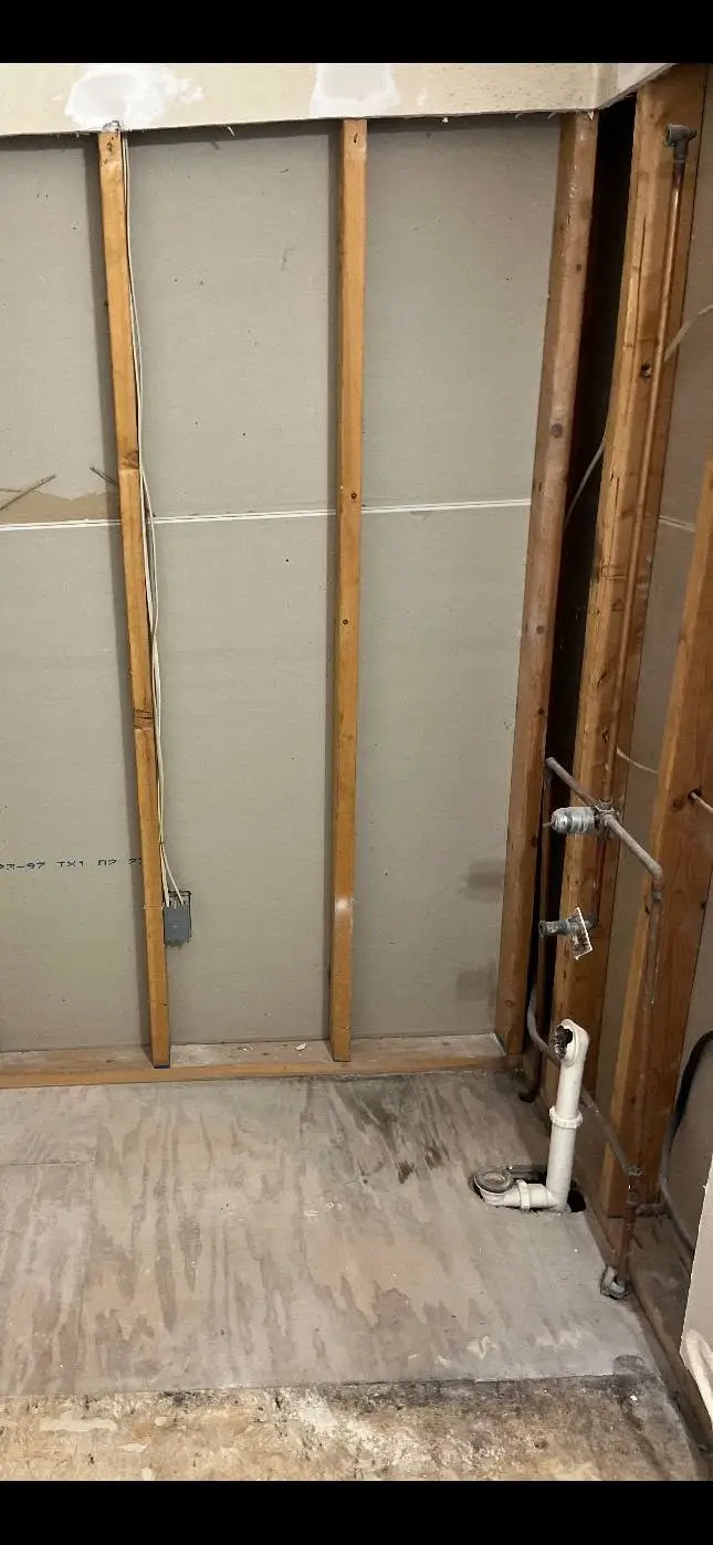 During: bath wall opened to the studs, with the supply lines and drain stack exposed above bare subfloor.