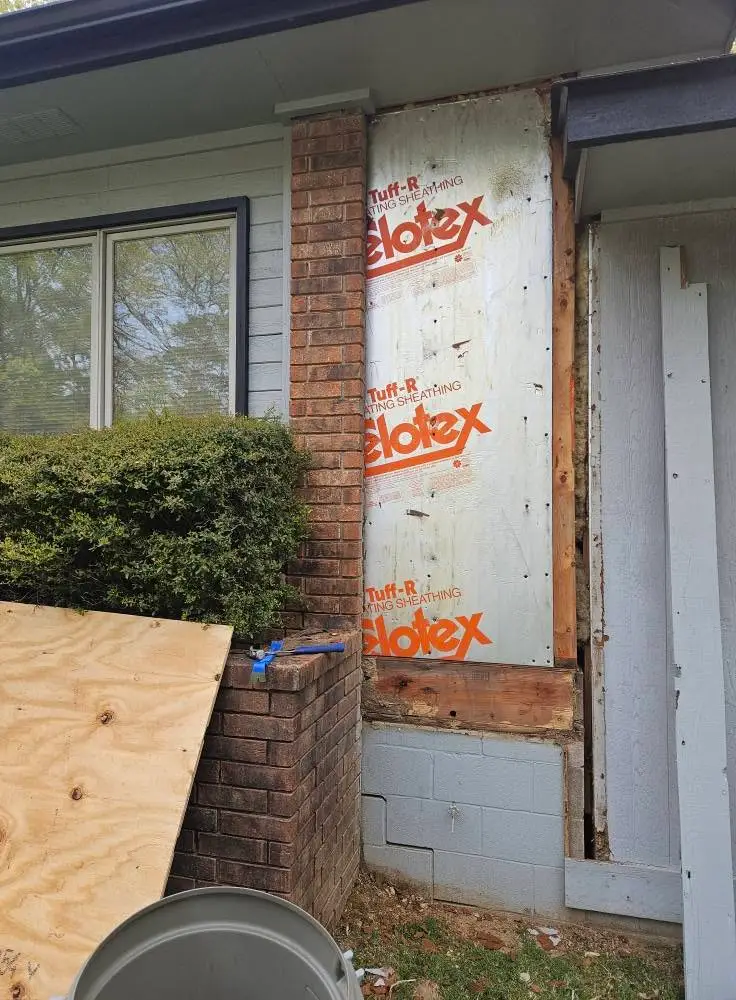 During: wall stripped to foil-faced insulating sheathing beside a brick chimney, with the rotted band board cut out.