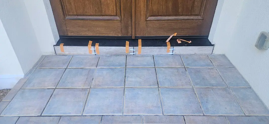After: flashed subsill under the entry doors carrying a new black threshold, shimmed and taped while the sealant sets.