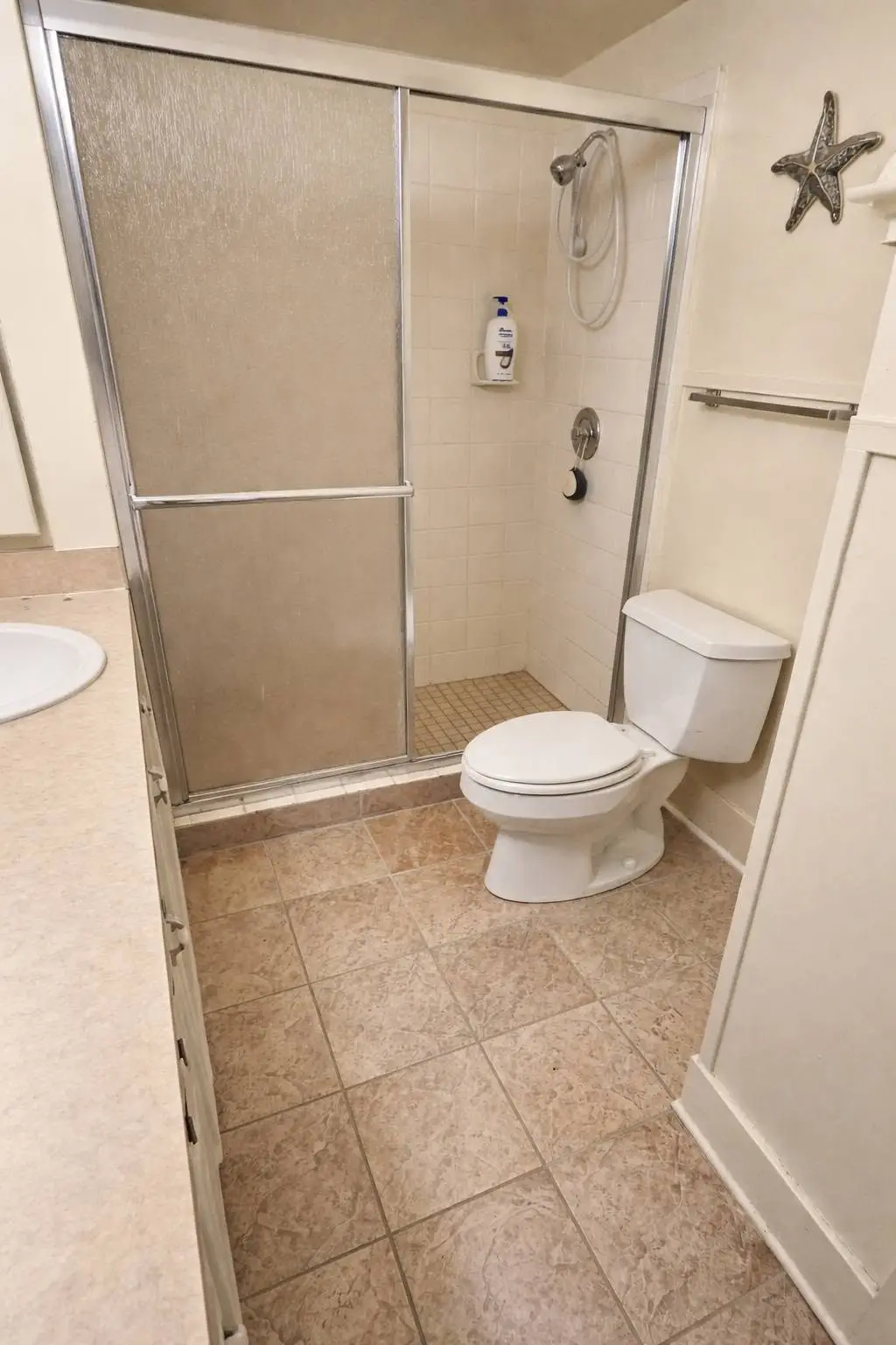 Before: framed sliding glass shower door over a tiled base, with the old sheet vinyl floor still down.