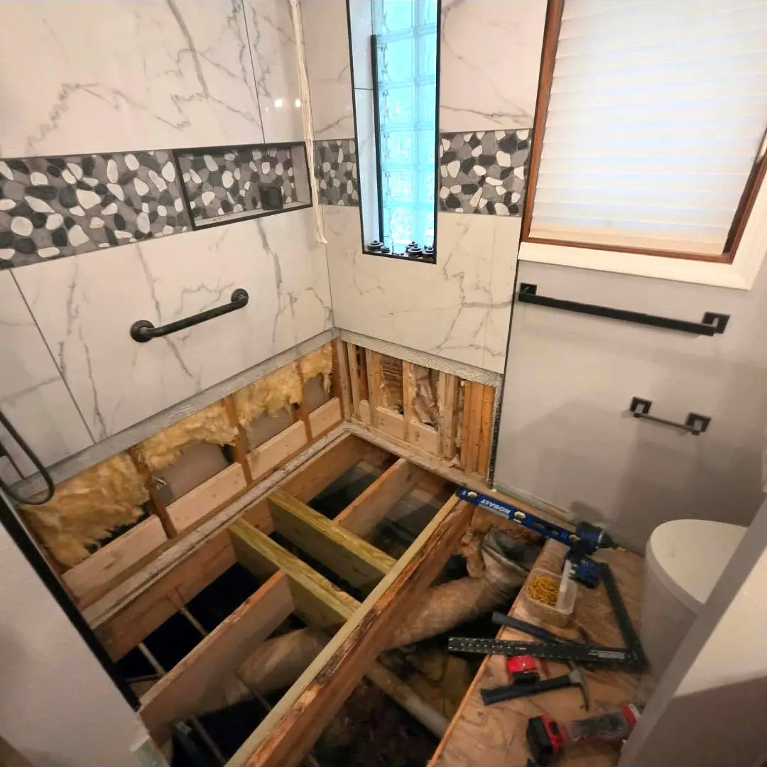 Before: open floor joists where the old shower pan and subfloor came out, tile still standing on the walls above.