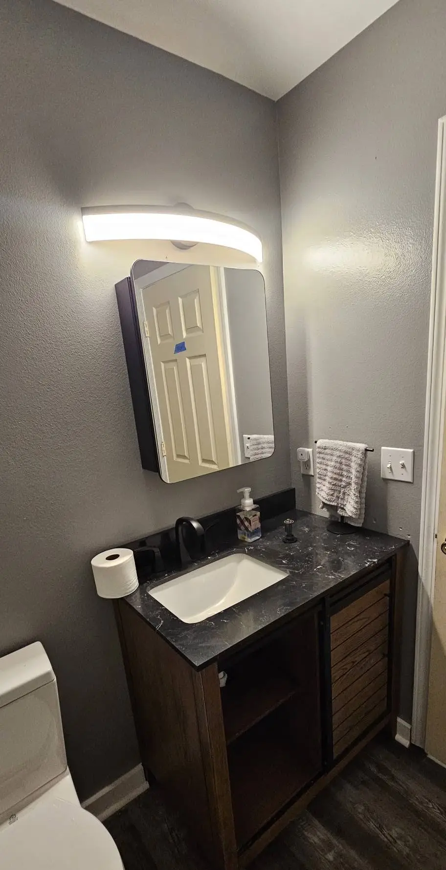 After: dark wood vanity set and plumbed under a stone top, with a mirrored medicine cabinet above.