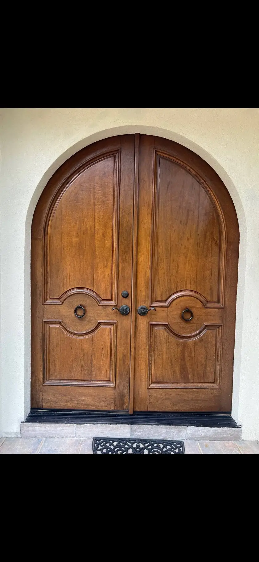 After: arched double entry doors in stained wood, hung square in a plaster arch with round centre pulls.