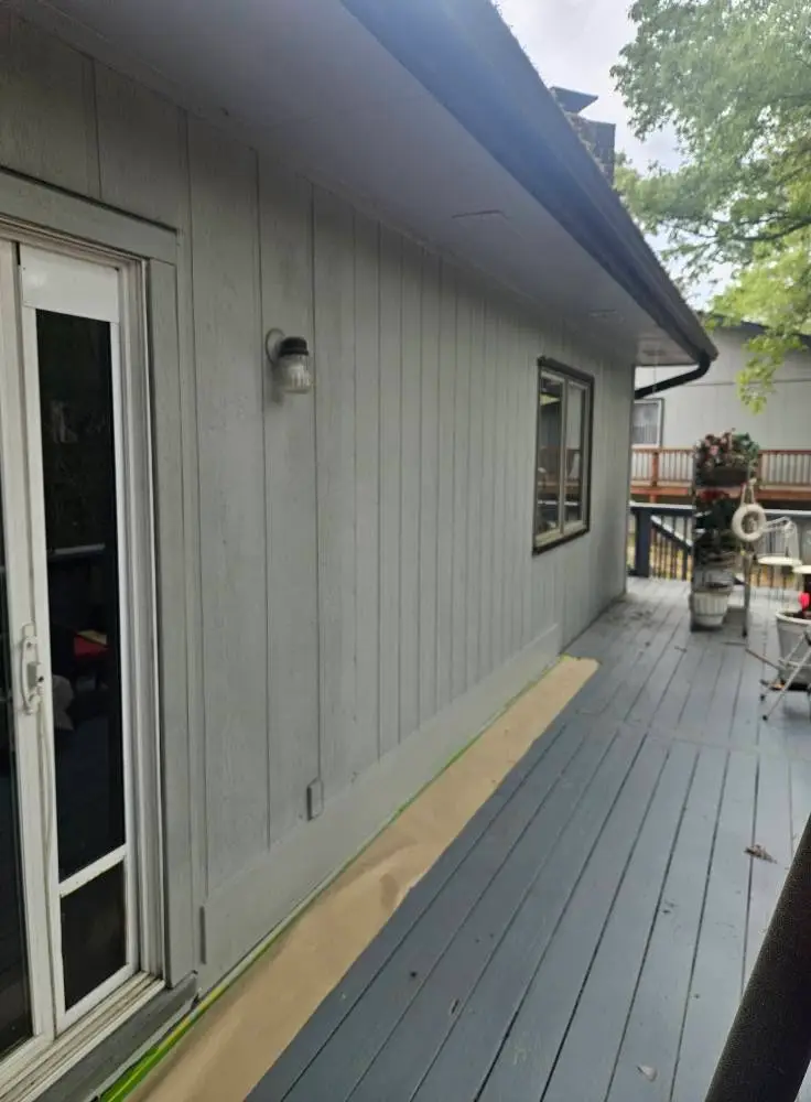 After: vertical groove siding along the deck wall painted light gray, with the sill line freshly masked.