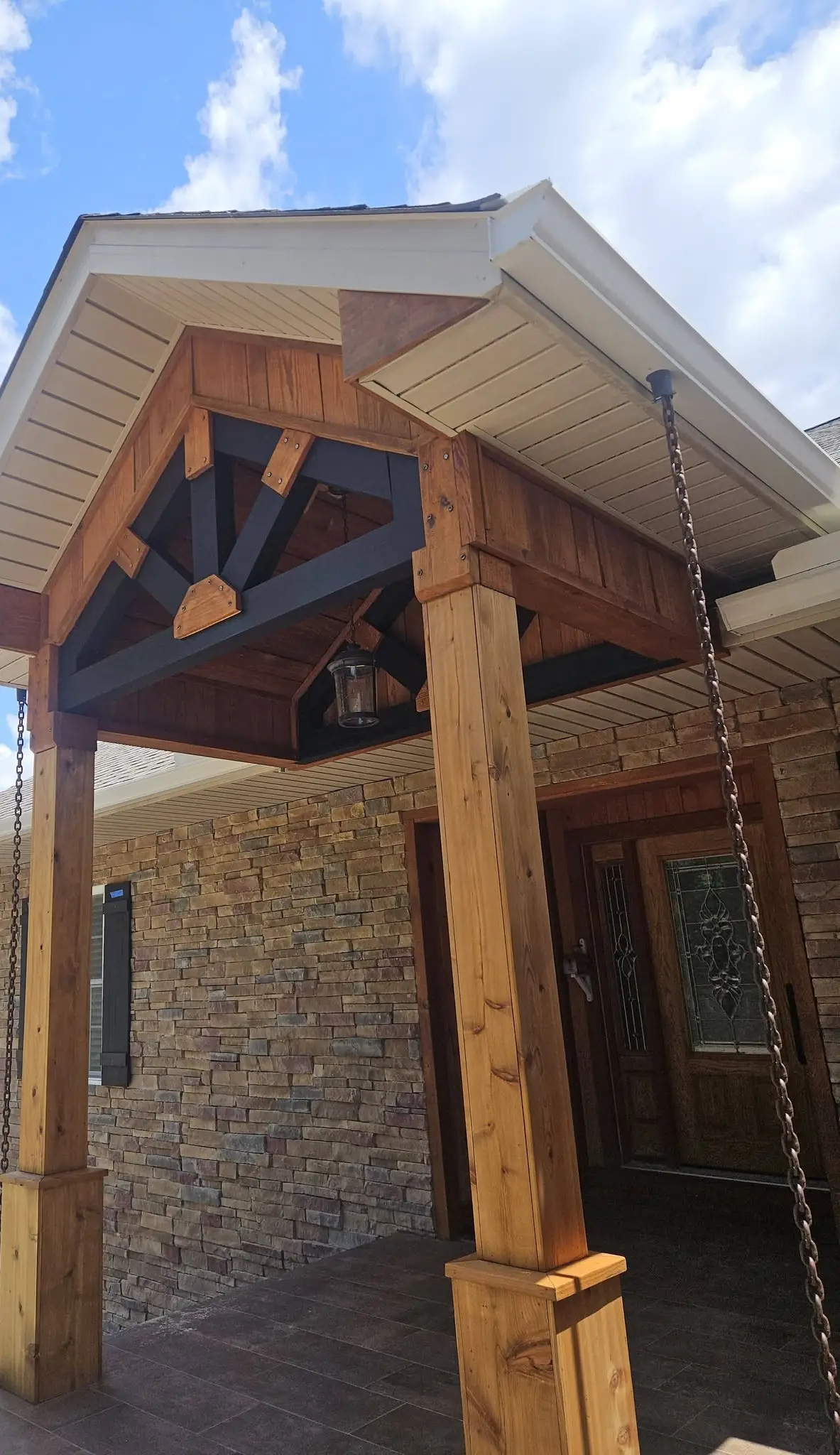 After: stone entry portico with the cedar posts and trusses stained warm brown and the braces painted black.