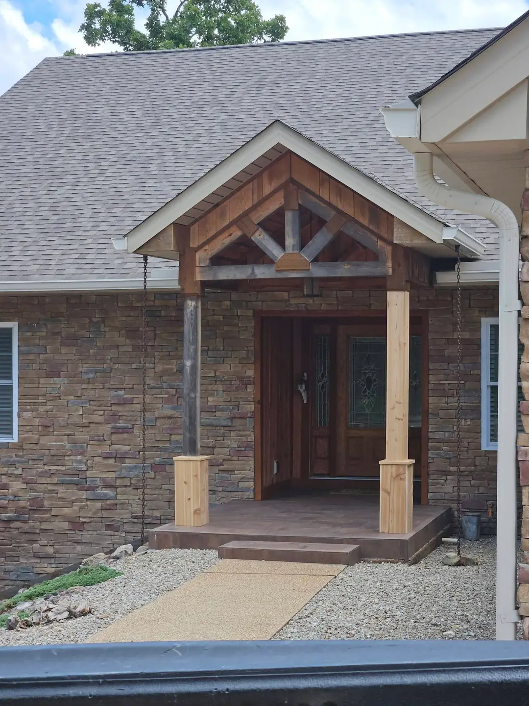 Before: raw cedar posts and gray timber trusses on a stone entry portico, unstained and unsealed.