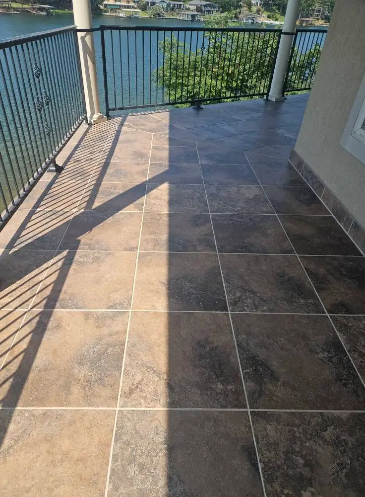 After: lakeside balcony tile with clean light gray grout in every joint, under black metal railing.