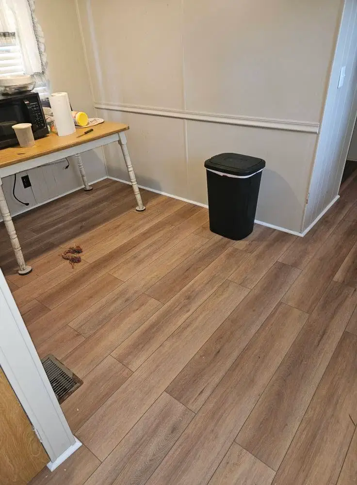 After: light oak LVP laid across a kitchen corner, with new white baseboard against the panelled wall.
