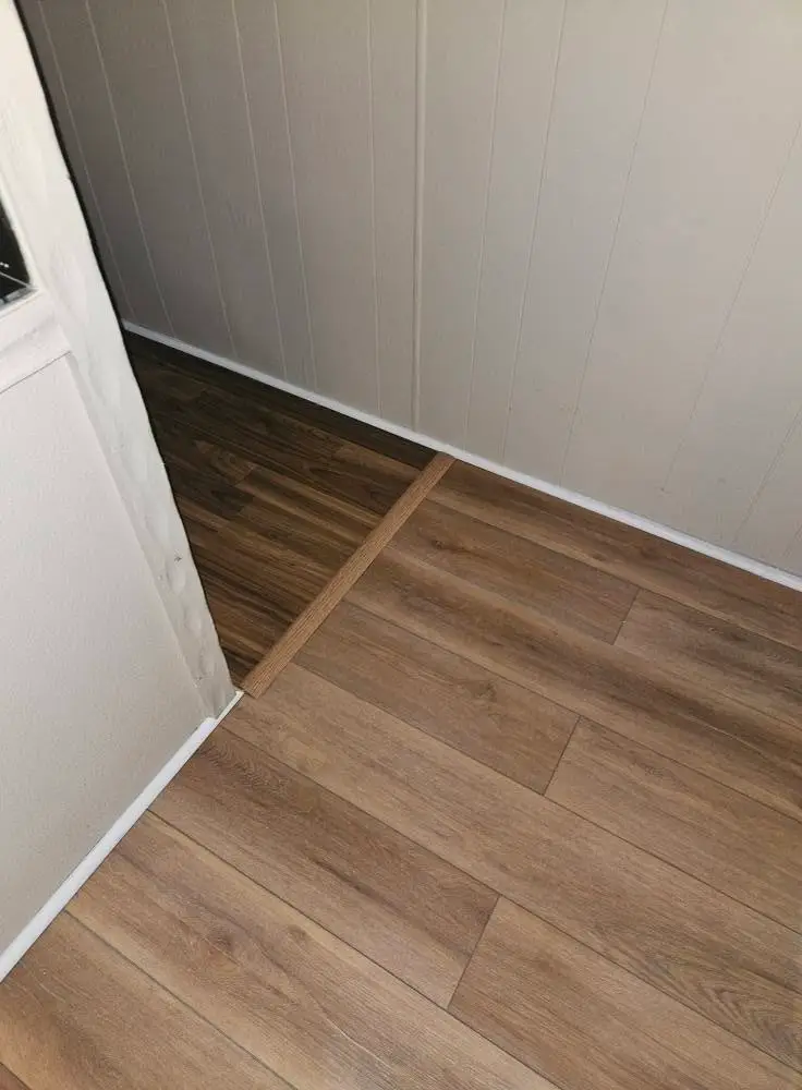 After: light oak LVP running through a doorway on a wood transition strip, with new white baseboard.
