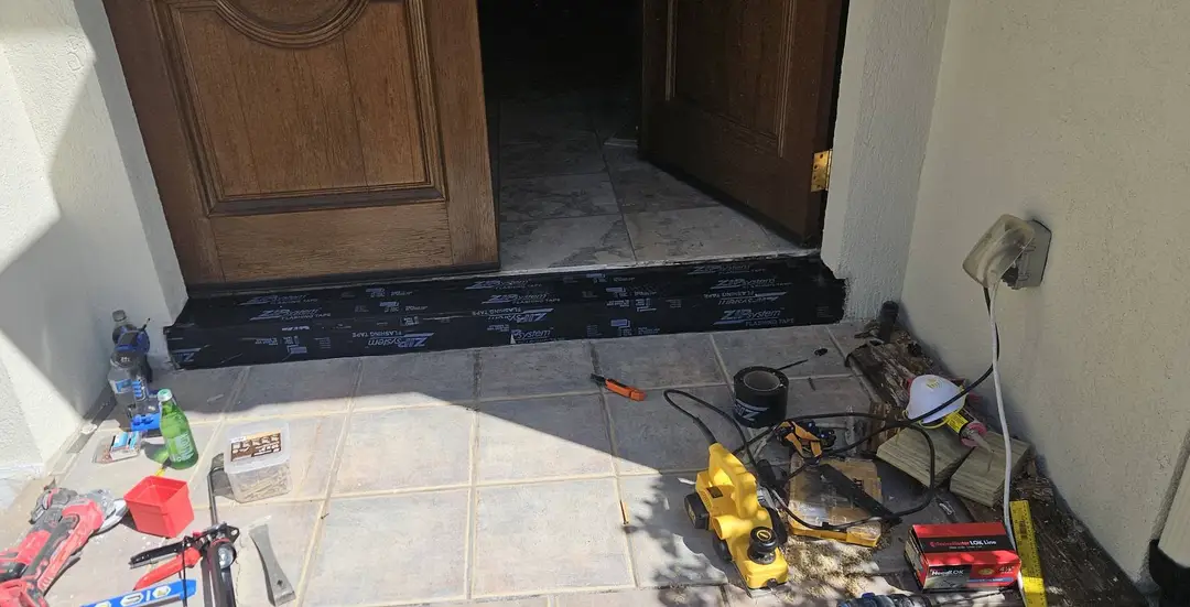 Before: rotted entry sill cut out under the doors, with the old threshold gone and the tile porch open.