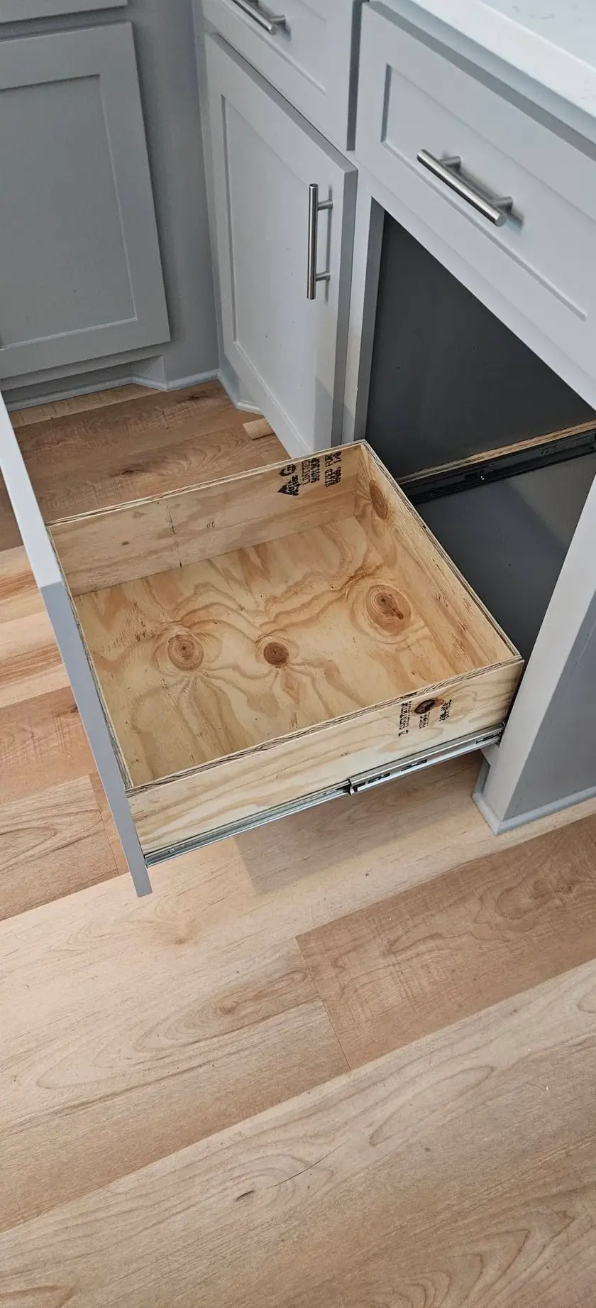 After: plywood pull-out trash drawer running out on full-extension slides inside a gray base cabinet.