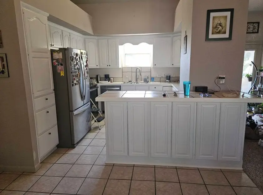 After: whole kitchen with every cabinet face painted white, from the tall pantry through to the tile-topped peninsula.