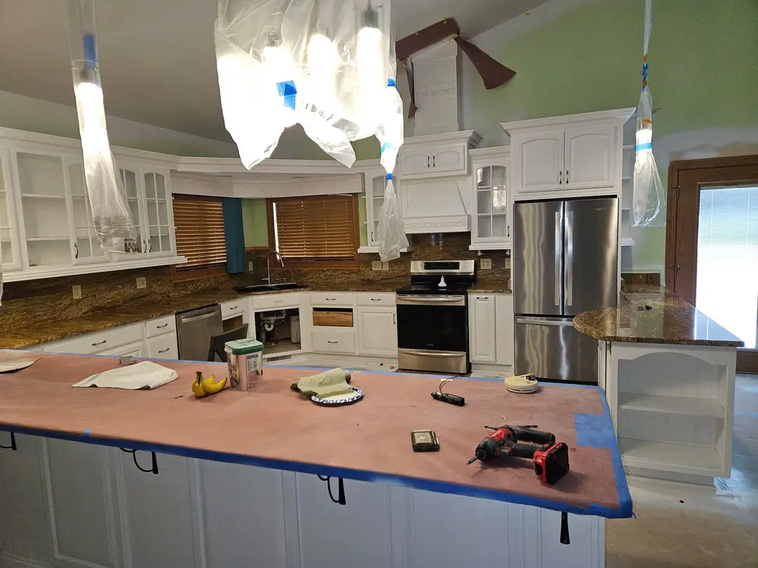 During: kitchen cabinets sprayed white around a stainless range and refrigerator, granite counters papered over.