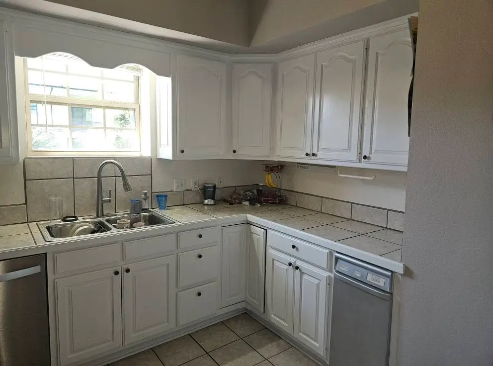 After: L-shaped kitchen with arched cabinet doors painted white above tile counters.