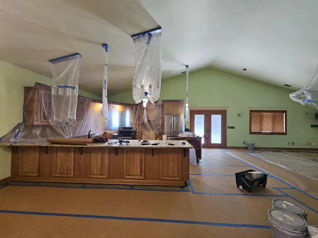 Before: oak peninsula and wall cabinets masked in plastic sheeting under a vaulted ceiling, ready for spray.