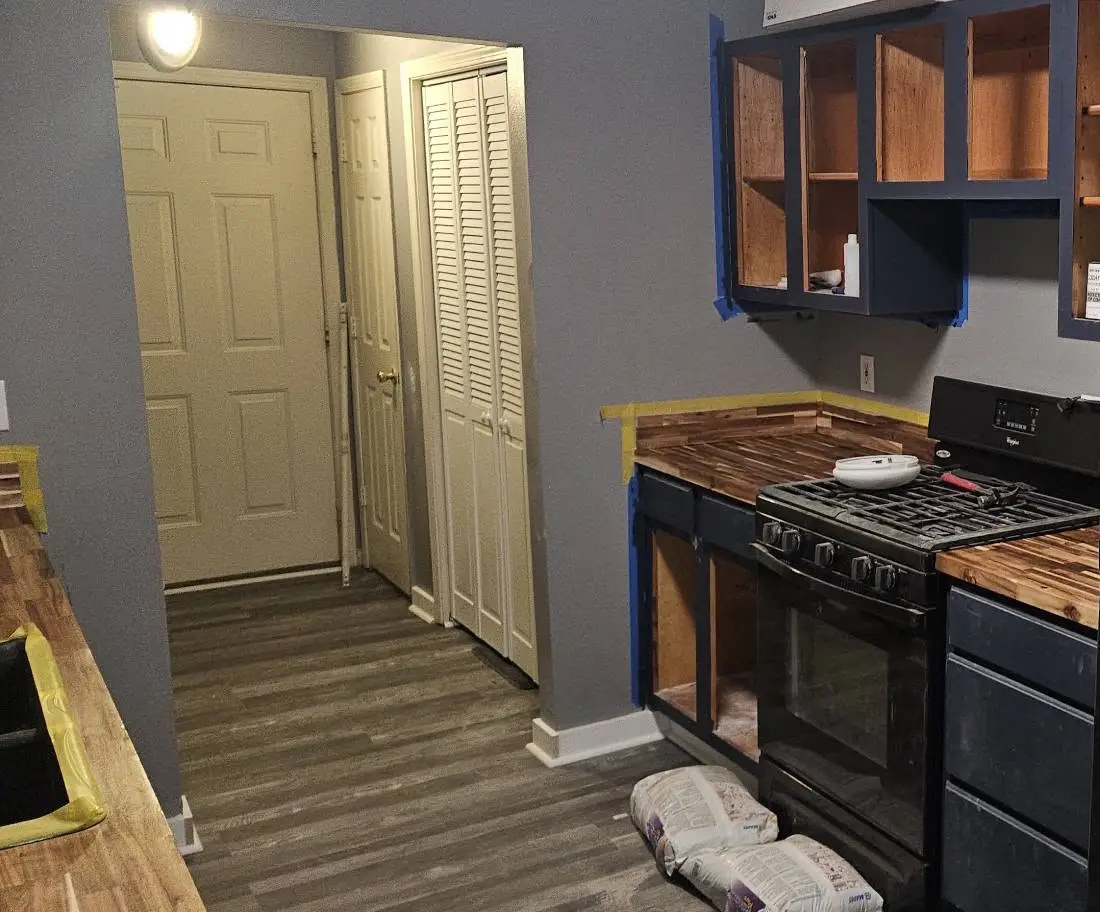 Before: navy cabinet boxes taped off with the doors removed, above a butcher block counter and a gas range.