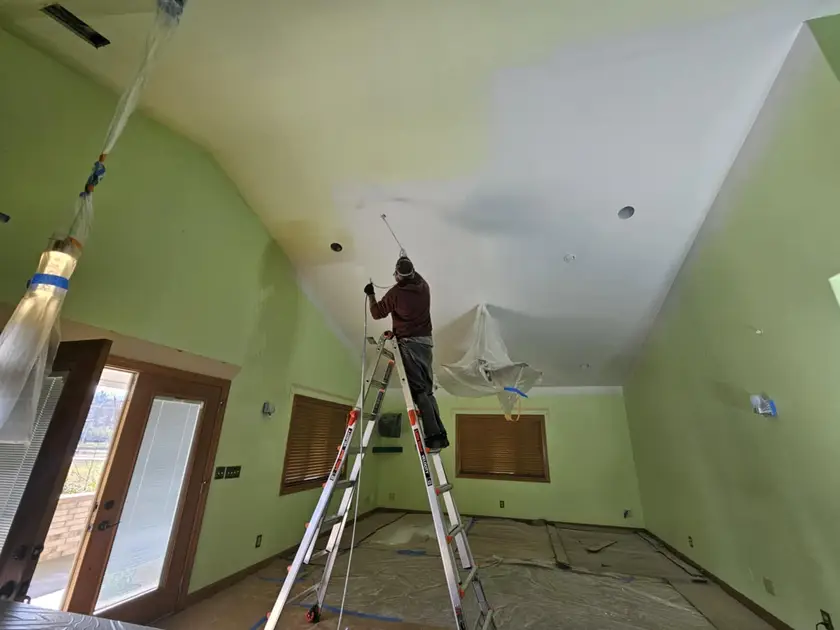 During: vaulted ceiling rolled white above green walls, with light fixtures bagged and the floor papered.