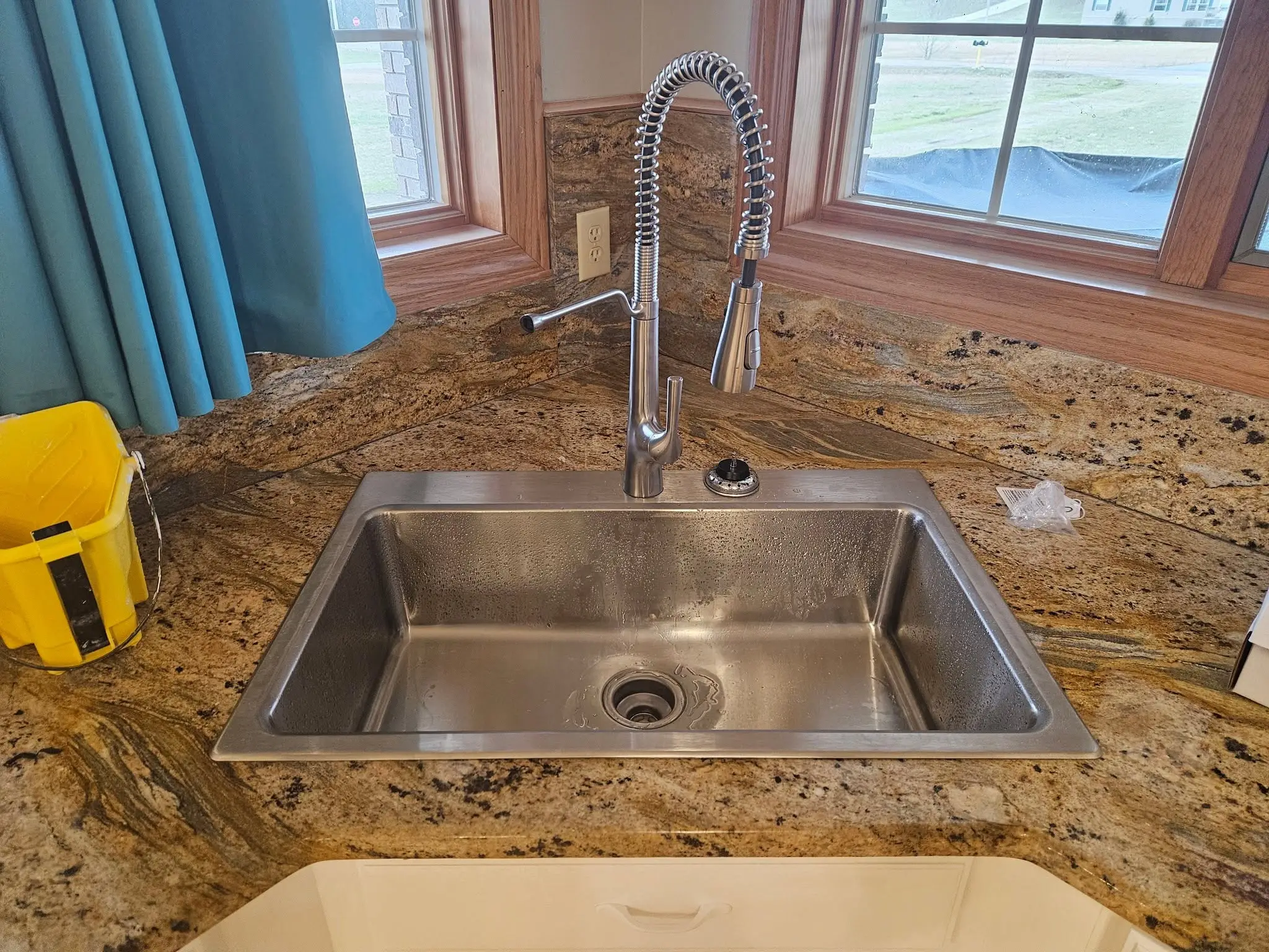 After: stainless drop-in sink set into granite with a pull-down spring faucet.