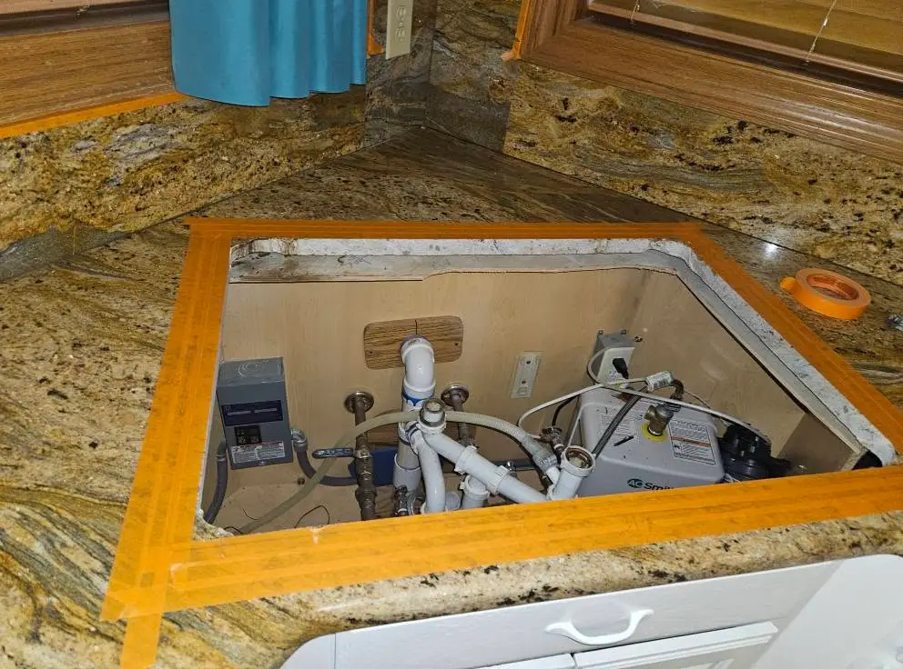 Before: taped granite cutout open to the supply lines, drain trap and disposal below.