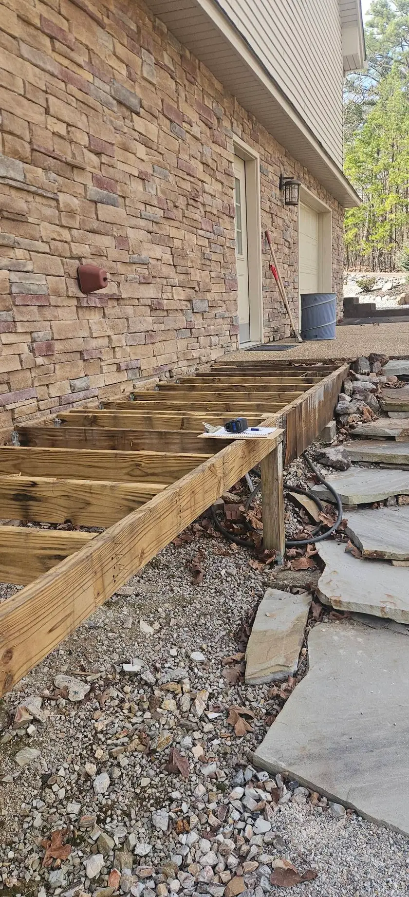 Before: open joists and a rim beam framed along a stone wall, with the ledger bolted and no decking down.