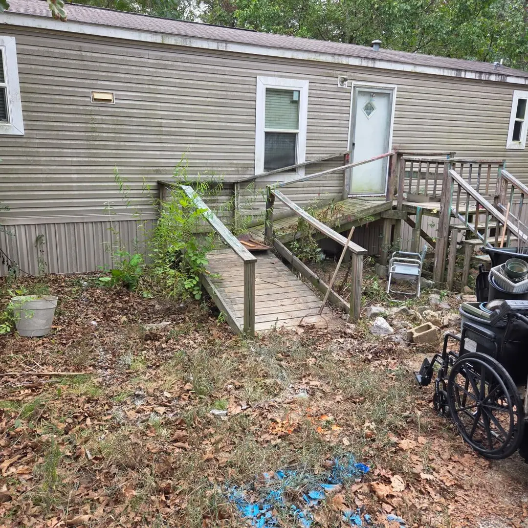 Before: a weathered wood ramp and stair at the door of a manufactured home, with weeds grown up through the railing.