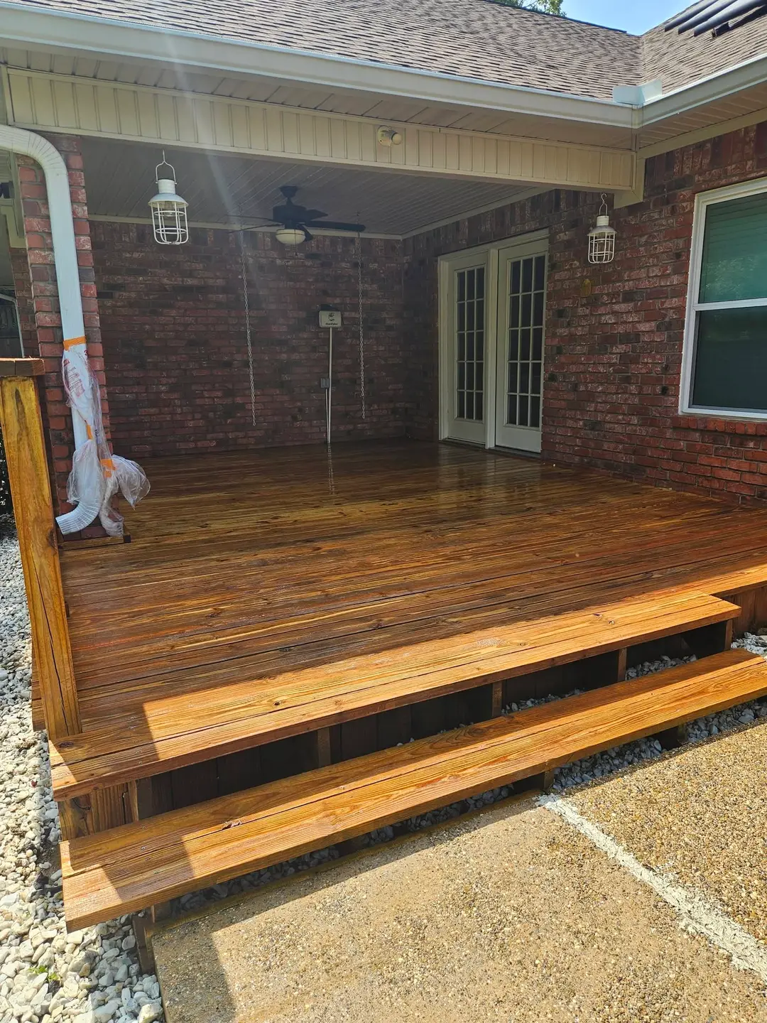After: covered patio deck finished deep brown, with two wide steps down to the concrete pad.
