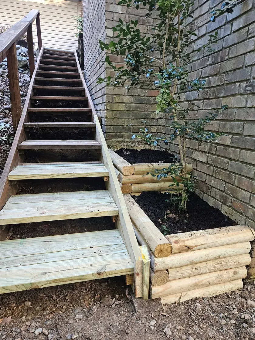 After: new treated stair stringers and treads beside a timber-walled planting bed filled with dark mulch.