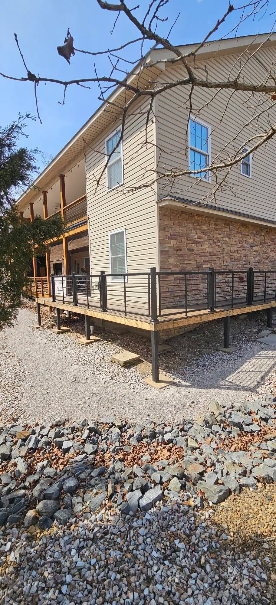 After: composite walkway wrapping the corner of the house on steel posts, with black metal railing.
