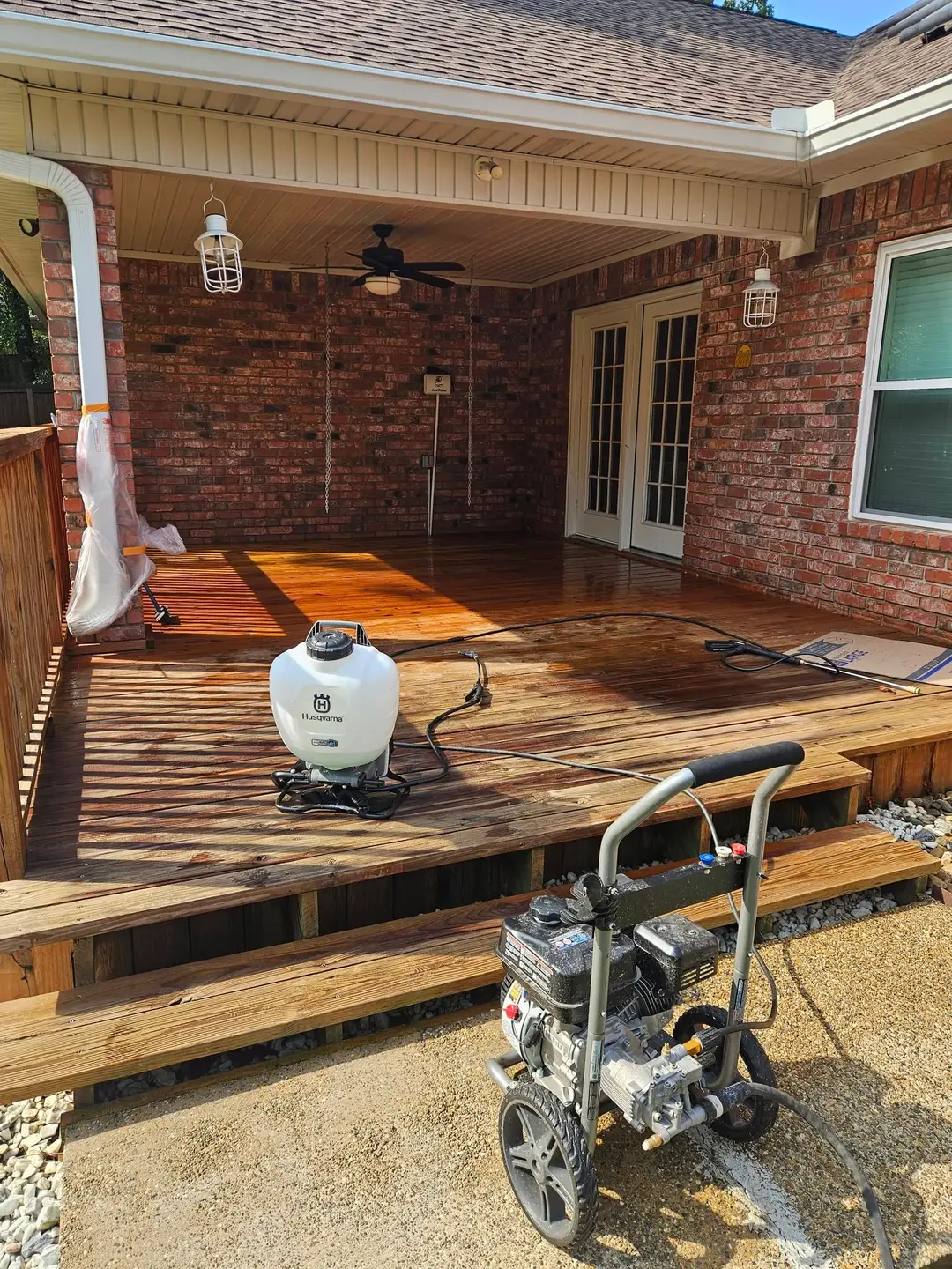 During: covered brick patio deck soaked from pressure washing, with the washer and sprayer still on the boards.