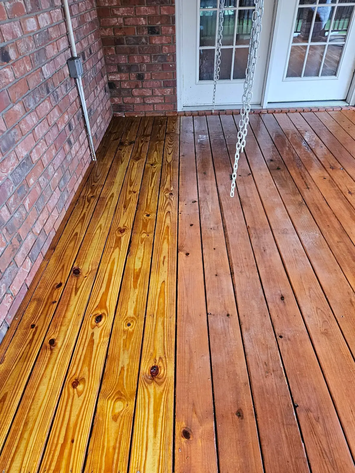 After: porch boards stained warm amber, the grain reading clean right up to the brick wall.