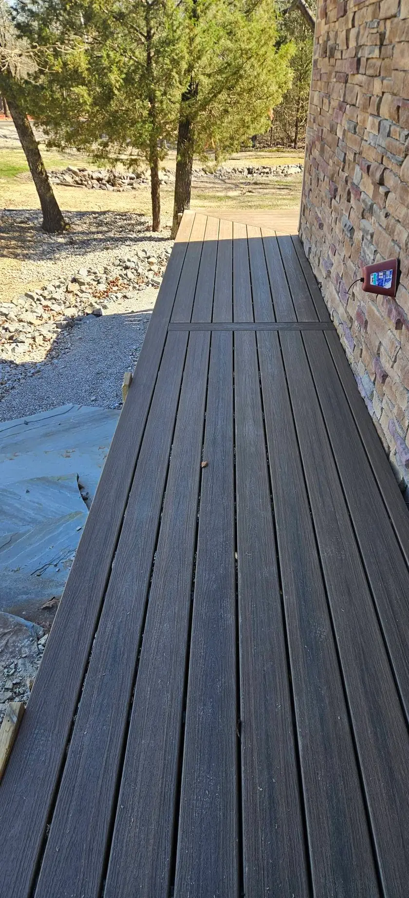 After: dark gray composite walkway running the length of the stone wall, boards picture-framed at the edge.