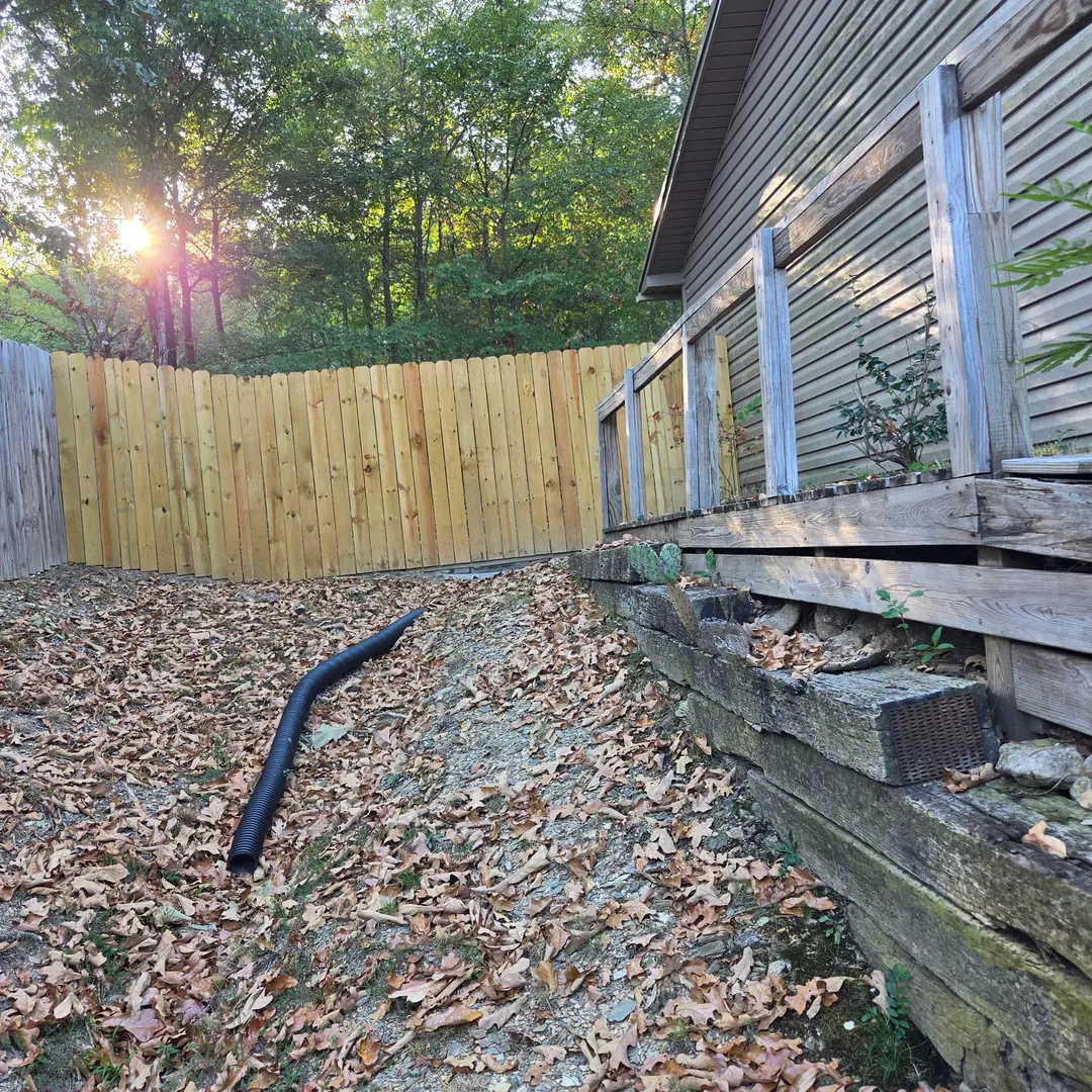 Before: bare dirt and leaf litter beside a deck, with a corrugated downspout extension running across the slope.