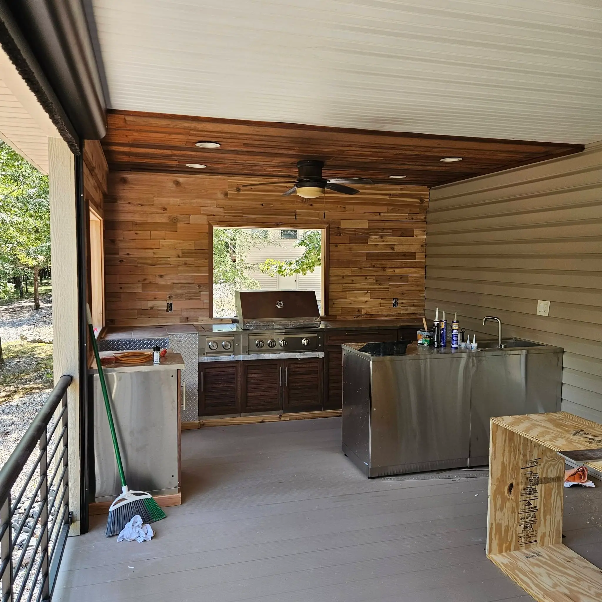 After: cedar plank outdoor kitchen with a built-in gas grill and a stainless counter run under a pass-through window.