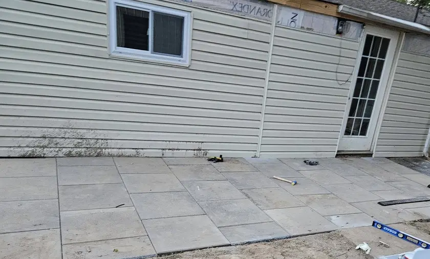 After: large-format paver patio laid tight against the building, with the field swept and the edges set.