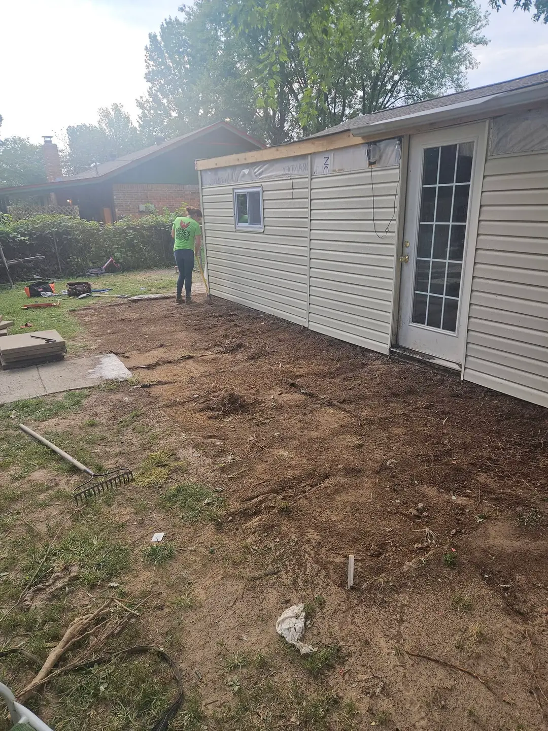 Before: bare dirt raked flat along a new-sided outbuilding, graded for the paver patio to come.